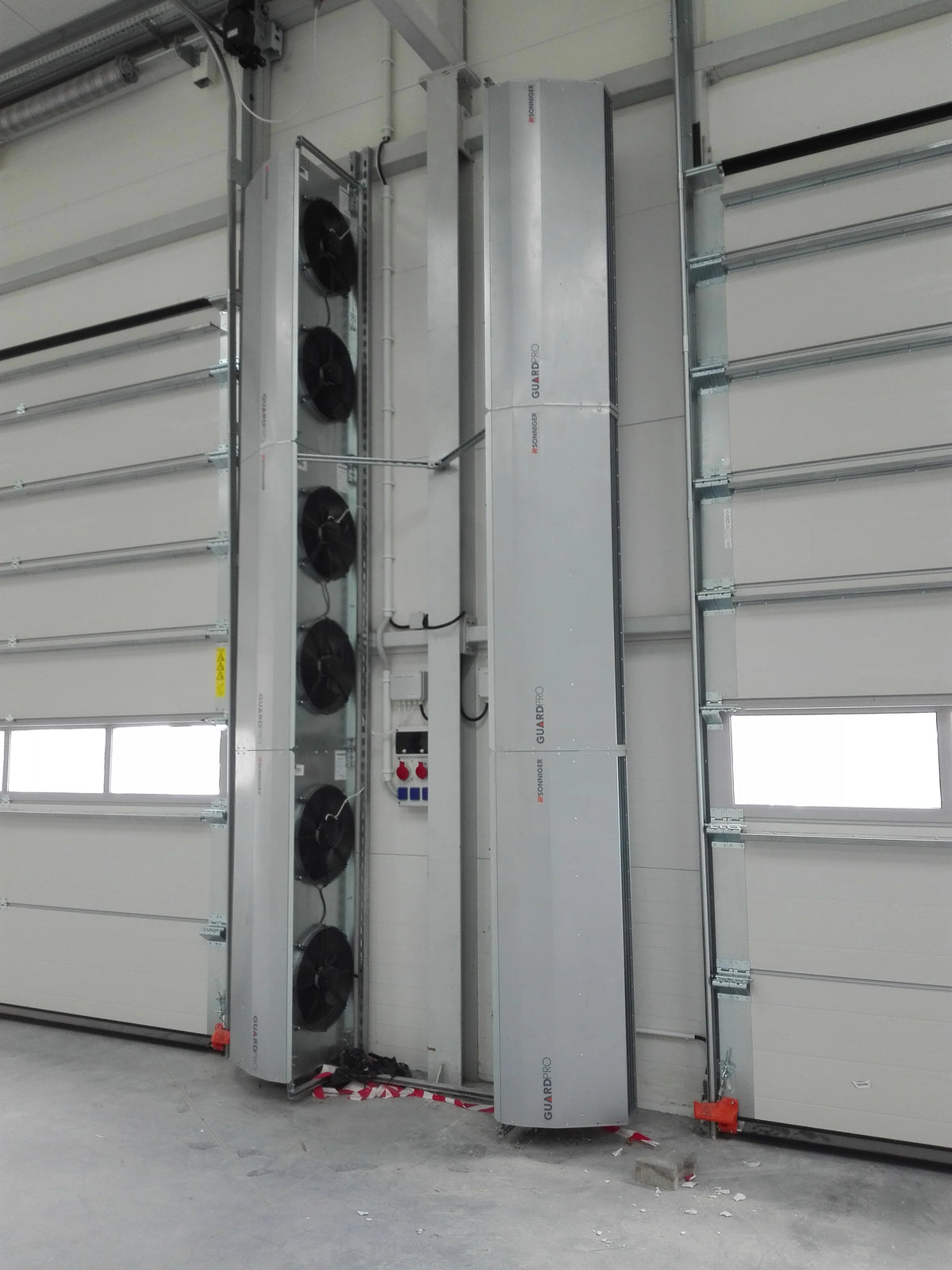 Rideau d'air chaud verticale GUARD PRO à proximité de portes sectionnelles en entrepôt 
